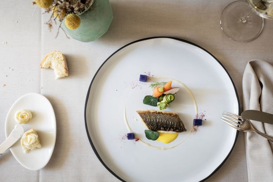 Fischgericht mit Butter, Brot, Weinglas und Blumenvase auf einem schön gedeckten Tisch. ©Löwengrube/Alex Filz