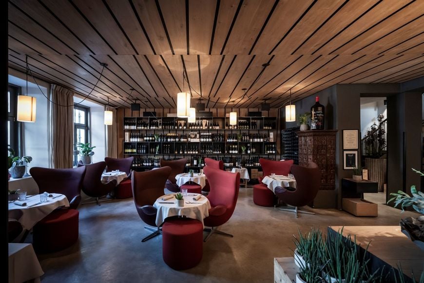 Innenbereich des Restaurants mit gedeckten Tischen, gemütlichen Sesseln und großem Weinregal im Hintergrund. ©Löwengrube/Alex Filz